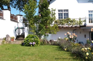 Ferienwohnung Zauberhaft - Außenansicht mit grüner Wiese, Blumen, Terrasse und Balkon